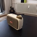 Bílý přenosný reproduktor s látkovým potahem v béžovo-černé barvě. Na přední straně je červený obdélníkový štítek s bílým nápisem Positive Grid. Na h…