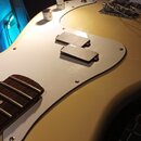 Detail elektrické kytary v krémové barvě s bílým pickguardem. Na pickguardu jsou umístěny dva černé humbuckery, vedle nich jsou dvě ovládací knoflíky…