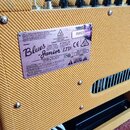Detail zadní strany kytarového komba s žlutým texturovaným povrchem. Na přístroji je nalepený stříbrný štítek s nápisy MODEL Blues Junior LTD a FENDE…