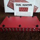 Červený kovový pedalboard s osmi stoupacími spínači. Na horní straně jsou čtyři černé knoflíky a na zadní straně řada konektorů s nápisy RETURN, OUTA…
