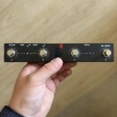 Černý obdélníkový přístroj s kovovým povrchem a čtyřmi konektory. Na horní straně jsou nápisy (U O H), USB, HOST a PEDAL, v pravém rohu je logo M-VAV…