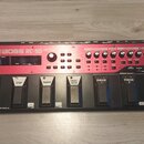 Červený loop pedal značky BOSS s označením RC-50. Zařízení má horní ovládací panel s několika knoflíky, tlačítky a malým displejem vlevo. Ve spodní č…