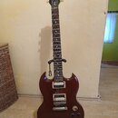 Tmavě hnědá elektrická kytara s dvojstupňovými humbuckery, umístěná na černém stojanu. Na hlavě nástroje je bílý nápis Gibson a pod ním v kurzivě Epi…