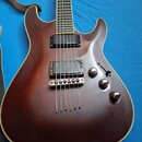 Hnědá elektrická kytara s dvojstupňovými humbuckery a chromovaným mostem. Na těle jsou tři otočné knofíky a jeden přepínač poloh snímačů. Povrch lako…