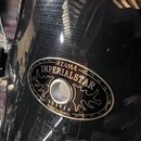 Detail černé lesklé povrchové vrstvy bubnu s kovovým kováním. Na nástroji je oválný štít s nápisy TAMA, IMPERIALSTAR a MADE IN CHINA. Pod středovým o…