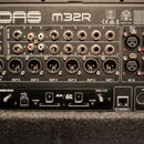 Zadávací panel digitálního mixeru s nápisem MIDAS M32R. Jsou zde viditelné různé typy konektorů, včetně XLR, jack 6,35 mm a USB. V dolní části je mod…