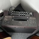 Hnědý akustický zesilovač s nápisem MOOGER a označením modelu SDSØA ACOUSTIC AMPLIFIER. Horní panel obsahuje ovládací knoflíky, přepínače a vstupy, z…