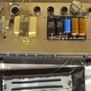 Fotografie zachycuje vnitřek elektronického zařízení s kovovým šasi zlatavé barvy. Uvnitř jsou vidět transformátory, kondenzátory a řada konektorů v…