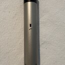 Stříbrný cylindrický mikrofon s černou horní částí. Na černé části je viditelné číslo 50 a v dolní části těla nápis Made in Germany. Povrch je matný…