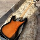 Zadní strana elektrické basové kytary s tělem v provedení sunburst (oranžová a černá). Na zadní straně těla je kovový štít s nápisem "Custom Shop". H…