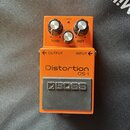 Oranžový kytarový efekt s nápisem Distortion DS-1 a logem BOSS na šedém spínacím pedálu. Na horní straně jsou tři ovládací knoflíky s popisky TONE, L…