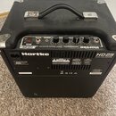 Černý basový kombo zesilovač značky Hartke, model HD25 (nápis 25 WATT BASS AMPLIFIER). Na horní ovládací ploše jsou čtyři otočné potenciometry, červe…