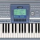 Stříbrný digitální klavír s černými a bílými klávesami. V horní části je umístěn modrý ovládací panel s displejem a nápisem YAMAHA. V pravé části nad…