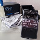 Na fotografii je kytarový pedál Boss IR-2 Amp & Cabinet v modré barvě s černým spodním panelem. Vedle pedálu je umístěna originální černá krabice s n…