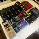 Sestava efektů pro basovou kytaru rozložená na bílém stole. Jsou zde pedály značek TC HELICON (model VOCALIVE), DigiTech (Whammy), Boss (modely MT-2…