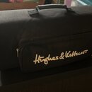 Černá látková přepravní taška s rukojetí a zipovými kapsami. Na přední kapse je žlutý nápis Hughes & Kettner. Taška leží na černém kytarovém zesilova…