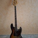 Elektrická basová kytara s tělem v provedení sunburst a hnědým hmatníkem. Na hlavě je viditelné logo Fender a nápis Jazz Bass. Kytara má tmavý pickgu…