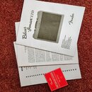 Fotografie zobrazuje několik listů papíru a červenou kartu na červeném koberci. Na horním listu je obrázek kytarového komba a nápisy Blues -Junior™LT…