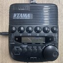 Černý rytmický doprovod TAMA RHYTHM WATCH RW200 s digitálním displejem a ovládacími tlačítky. Na horní části je nápis TAP TEMPO a vprostřed logo TAMA…