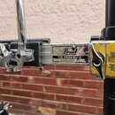 Detail části černého bubnového systému s kovovými spojovacími prvky. Na středovém kovovém štítku je nápis Pearl a THE DRUM RACK, v dolní části drobný…