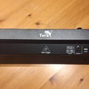 Černý lineární reproduktor s dřevěnými bočními panely. Na horní straně je bílý nápis Toro s ikonou tygra, na zadní straně logo a nápis behringer. Zad…