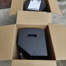 Dvě černé reproduktorové bedny umístěné v kartonových krabicích. Na horním reproduktoru je položen bílý papírový návod s nápisem DRM. Povrch reproduk…