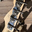 Zadní strana hlavy basové kytary z přírodního dřeva s chromovanými ladicími kolíky. Na dřevě je nápis: Designed and based by Fender Crafted in China…