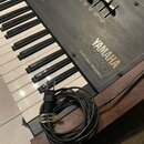 Černý elektronický klavír s bílými a černými klávesami. Na čelním panelu je nápis YAMAHA SK20 SYMPHONIC ENSEMBLE a řada posuvníků s popisky jako CUT…