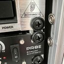 Detail dvou rackových zařízení v přepravním kufru. Horní přístroj má stříbrný brouškovaný povrch s logem BEHRINGER v trojúhelníku a nápisem POWER. Sp…