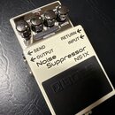 Bílý efekt pedál s černým nášlapným spínáčem a nápisem BOSS. Na horní straně jsou čtyři černé otočné ovratidla a nápisy CHECK, THRESHOLD, DECAY, REDU…