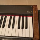 Detail digitálního piana s černým šasi a pravou bočnicí v imitaci dřeva. Na černé části je bílý nápis pRP7 a pod ním RealPiano. Nad klávesami jsou vi…
