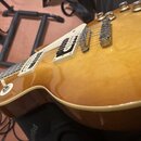 Detailní pohled na tělo elektrické kytary v žlutém gradientním lakování s bílým lemováním. Nástroj má dva humbuckery v krémových rámečcích, dvě tónov…