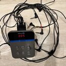 Šedý elektronický přístroj značky Millenium s červeným digitálním displejem, na kterém svítí číslo 005. Na přední straně jsou tlačítka Power, Select…
