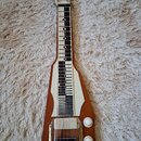 Elektrická kytara s hřidnicí typu lap steel v dřevěném provedení. Na hřidnici jsou viditelné bílé a černé značky poloh. V dolní části je umístěn sním…