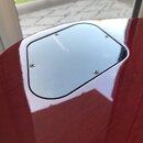Detail zadní strany kytary s červeným lakovaným povrchem. V horní části je umístěna světle šedá krytka s rounded hranami, která je připevněna čtyřmi…