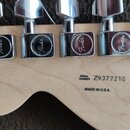 Zadní strana světlé dřevěné hlavy kytary s chromovanými ladičkami. Na každém z šesti ladiček je vyryto logo Fender. Na dřevě je černý nápis SERIAL NU…