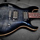 Elektrická kytara s tmavě modrým průsvitným lakem a viditelnou strukturou dřeva. Nástroj má dva humbuckery, stрійko typu Tune-o-matic a dvě ovládací…