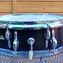 Černý snare drum s chromovanými obručmi a ladicími šrouby. Na korpusu je bílý nápis Amati v rukopisném stylu. Nástroj vykazuje známky používání a dro…