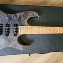 Elektrická kytara s šedým, mramorovaným povrchem těla a hnědým hmatníkem z dřeva. Na černé kytarové kufře pod nástrojem je bílý nápis CHAPMAN GUITARS…
