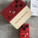Červený efekt pedál s nápisy BIG MUFF 2, DUAL OP-AMP a logem electro-harmonix podepsaným R.E. Meyer NEW YORK CITY, USA. Pedál má tři černé otočné kno…