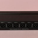 Černý rackový rozdělovač signálu s 16 výstupy typu XLR. Nad každým konektorem je bílý nápis OUTPUT 1 až OUTPUT 16. Na spodní hraně jsou nápisy Applie…