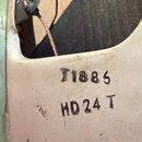Detail vnitřní části světle šedého kovového přístroje s viditelným elektrickým kabelem a pájenými spoji. Na povrchu jsou černé nápisy T1886 a HD24 T.…