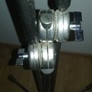 Detail kovového stojanu s teleskopickými trubkami a dvěma spojovacími klouby s utahovacími šrouby. Povrch kovu je matný a vykazuje známky opotřebení…