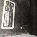 Detail černého povrchu s bílou kontrolní nálepkou. Na nálepce je logo Fender® a nápisy ELECTRONIC TEST, SOUND TEST a QUALITY ASSURANCE. V políčkách j…