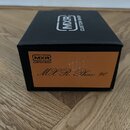Černá čtvrhlá krabička s oranžovou nálepkou na přední straně. Na horní části je bílé logo MXR a nápis CUSTOM SHOP. Oranžová nálepka obsahuje logo MXR…