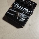 Černý kytarový efekt s bílým nápisem FuzzMo a podtitulem Fuzz Mode Ultra High Gain Distortion. Na spodní části je logo EBS. Zařízení má čtyři ovládac…