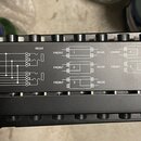 Detailní záběr na černý kovový panel s bílými technickými schématy zapojení. Jsou zde nápisy FRONT a REAR u různých diagramů, které jsou označeny pís…