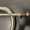 Detail stříbrného trombonu s viditelným opotřebením povrchu. Na lakovaném povrchu jsou četné žluté oděrky a škrábance, zejména v místě spoje s tahovk…