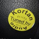 Kruhová žlutá nálepka s černým textem nalepená na černém povrchu z imitace kůže. Na nálepce je nápis Kortan Tuned by Audio a webová adresa www.kortan…