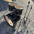 Černá bubnová sada s kovovým hardwarem, stojanem na činely a jedním činelem. Na basovém bubnu je vidět logo Mapex a nápis Mapex Drums. Na tomarech js…